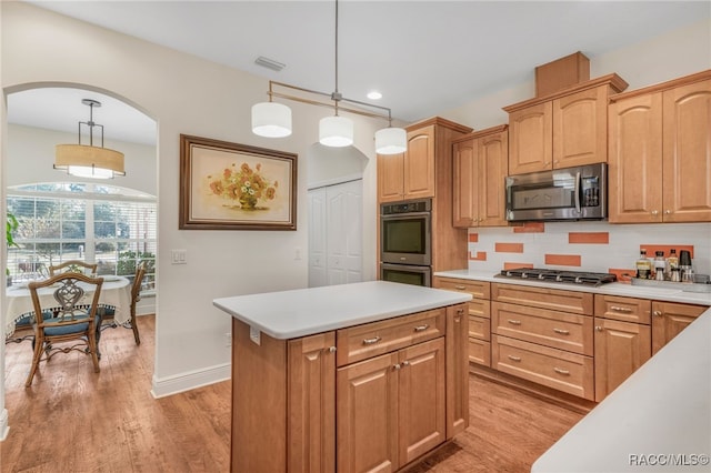 kitchen with appliances with stainless steel finishes, hanging light fixtures, tasteful backsplash, a kitchen island, and light wood-type flooring