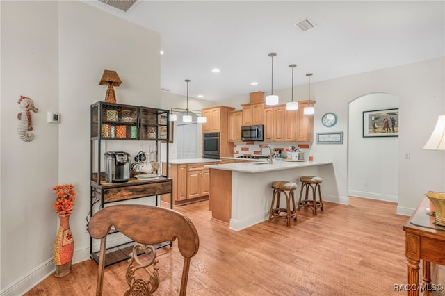 kitchen featuring appliances with stainless steel finishes, light brown cabinets, decorative light fixtures, kitchen peninsula, and light wood-type flooring