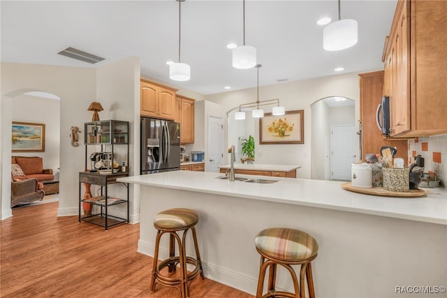 kitchen featuring a kitchen bar, sink, hanging light fixtures, light hardwood / wood-style flooring, and appliances with stainless steel finishes