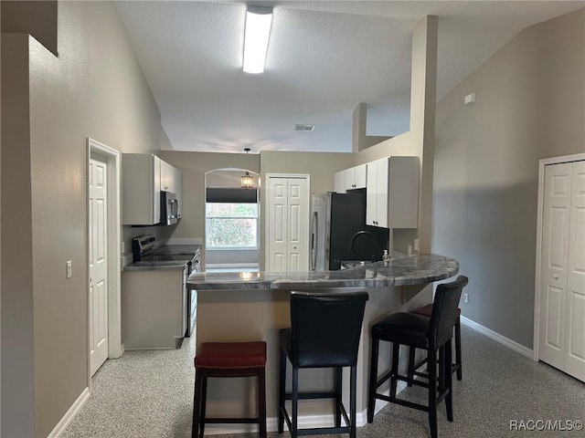 kitchen featuring kitchen peninsula, appliances with stainless steel finishes, a kitchen bar, light carpet, and lofted ceiling