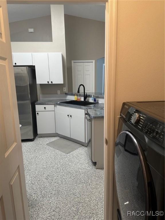 kitchen with lofted ceiling, white cabinets, sink, stainless steel fridge, and washer / dryer