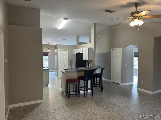 kitchen featuring white cabinets, a kitchen breakfast bar, ceiling fan, kitchen peninsula, and stainless steel refrigerator