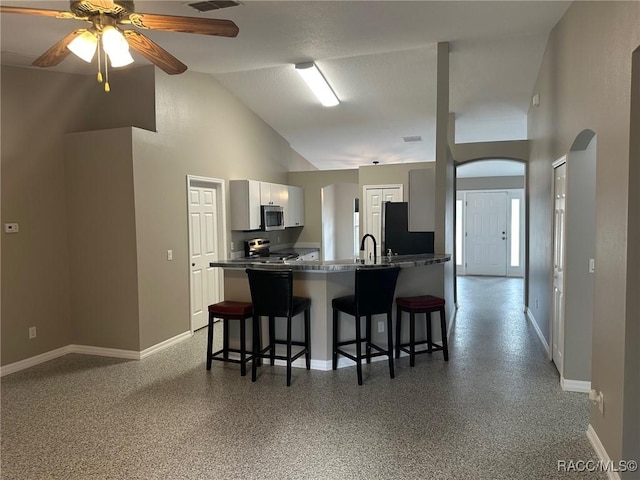 kitchen featuring high vaulted ceiling, kitchen peninsula, a breakfast bar, white cabinets, and appliances with stainless steel finishes