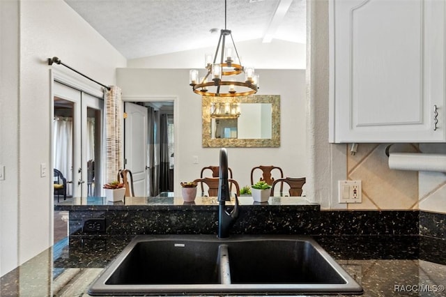 kitchen with a textured ceiling, vaulted ceiling, white cabinets, and a sink