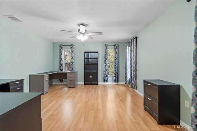 unfurnished office featuring a textured ceiling, light wood-style flooring, visible vents, and a ceiling fan