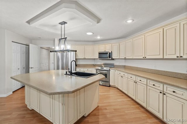 kitchen with hanging light fixtures, appliances with stainless steel finishes, light countertops, cream cabinetry, and a center island with sink