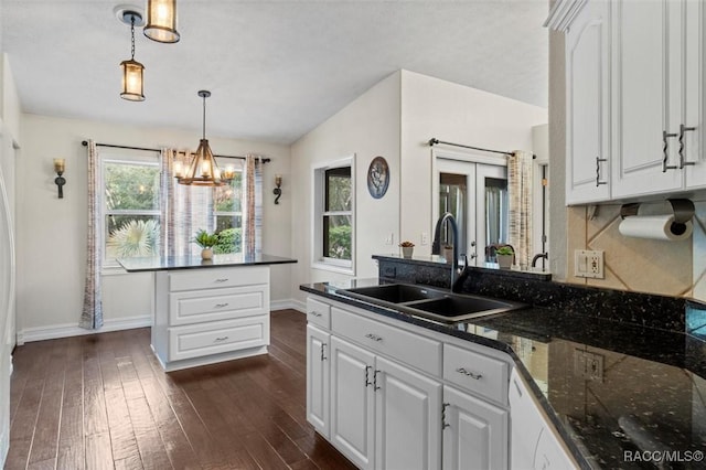 kitchen with dark wood-style flooring, a sink, white cabinets, dark stone counters, and pendant lighting