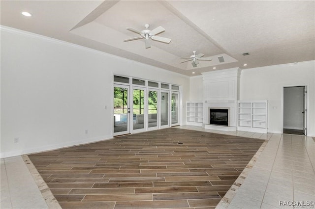 unfurnished living room with a raised ceiling, crown molding, ceiling fan, a fireplace, and wood-type flooring