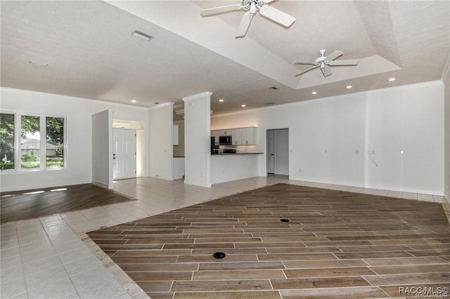 unfurnished living room with hardwood / wood-style floors, ceiling fan, crown molding, and a tray ceiling