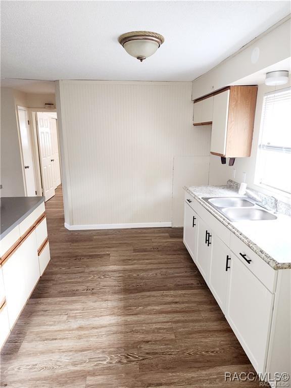 kitchen with a sink, light countertops, wood finished floors, and white cabinets