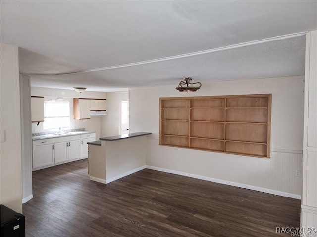 kitchen with dark wood-type flooring, white cabinets, a peninsula, and baseboards