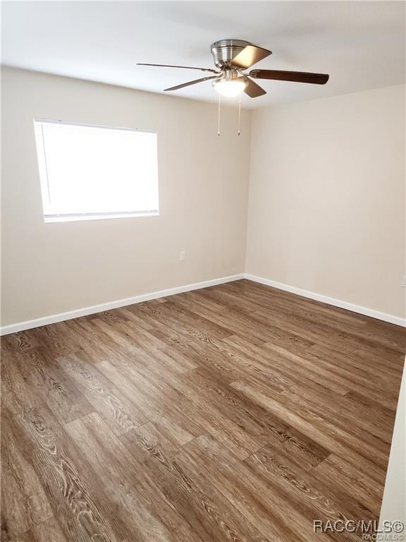 spare room with wood finished floors, a ceiling fan, and baseboards