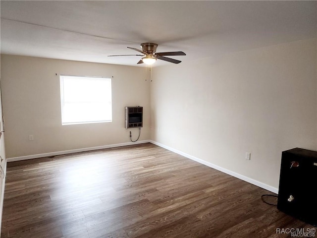 spare room with a ceiling fan, baseboards, heating unit, and wood finished floors