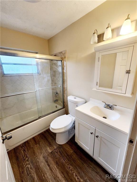 bathroom featuring toilet, shower / bath combination with glass door, wood finished floors, and vanity