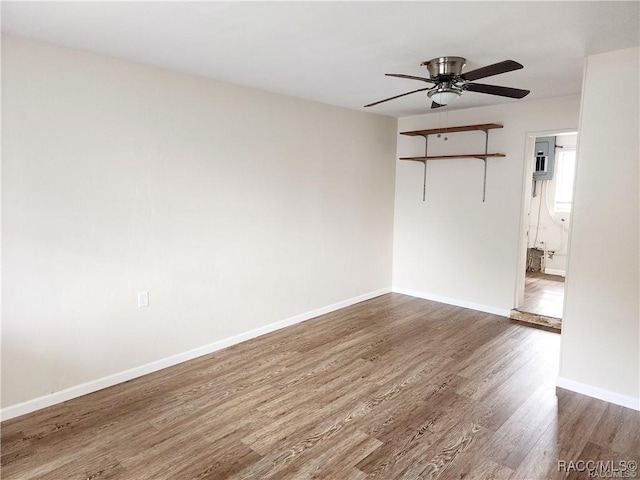 empty room featuring a ceiling fan, electric panel, baseboards, and wood finished floors