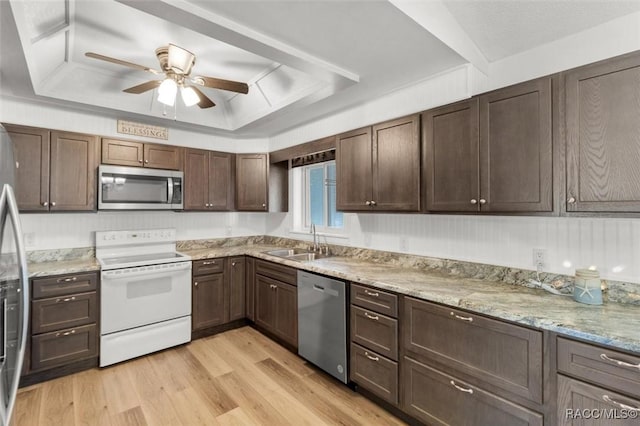 kitchen featuring a tray ceiling, appliances with stainless steel finishes, light wood-style floors, a ceiling fan, and a sink