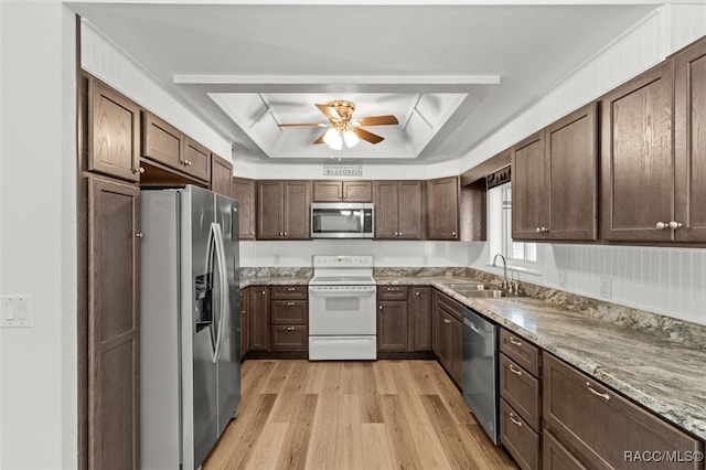 kitchen with a raised ceiling, appliances with stainless steel finishes, a sink, ceiling fan, and light wood-type flooring