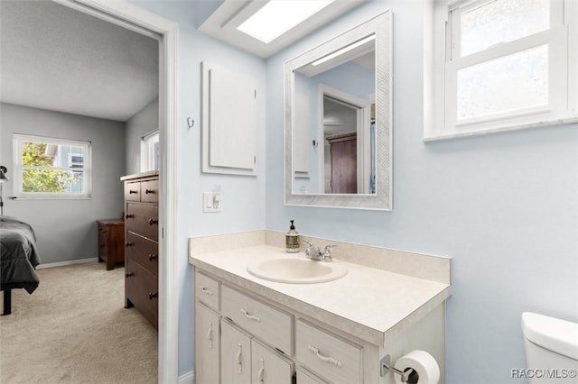 ensuite bathroom with toilet, connected bathroom, vanity, and baseboards