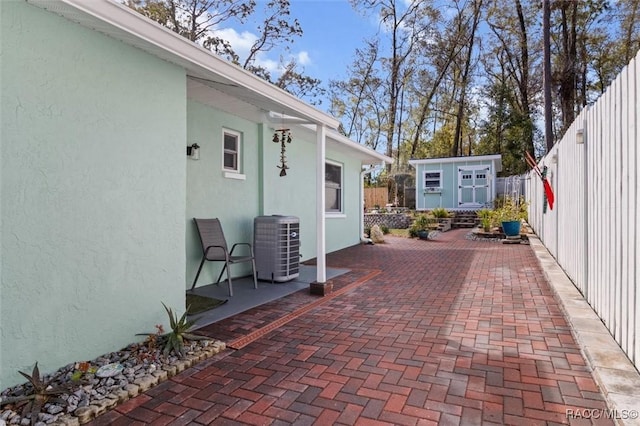 view of patio with an outbuilding, central AC unit, fence, and a storage unit