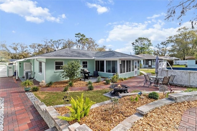 view of front of home with a patio, an outdoor fire pit, cooling unit, a sunroom, and stucco siding