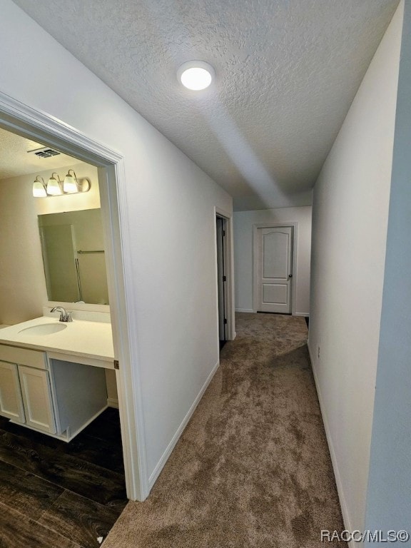 hall with dark carpet, sink, and a textured ceiling