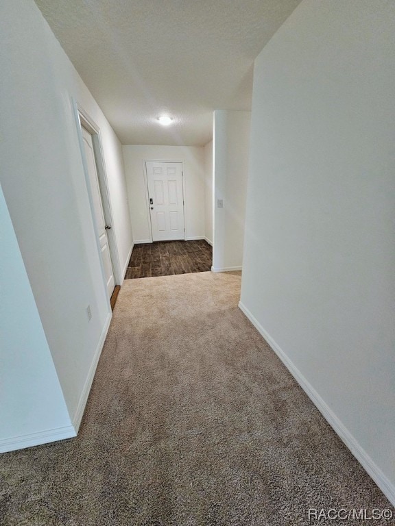 corridor featuring dark carpet and a textured ceiling