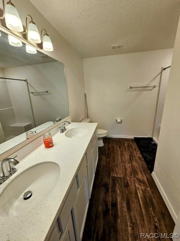 bathroom featuring vanity, a shower, hardwood / wood-style flooring, toilet, and a textured ceiling