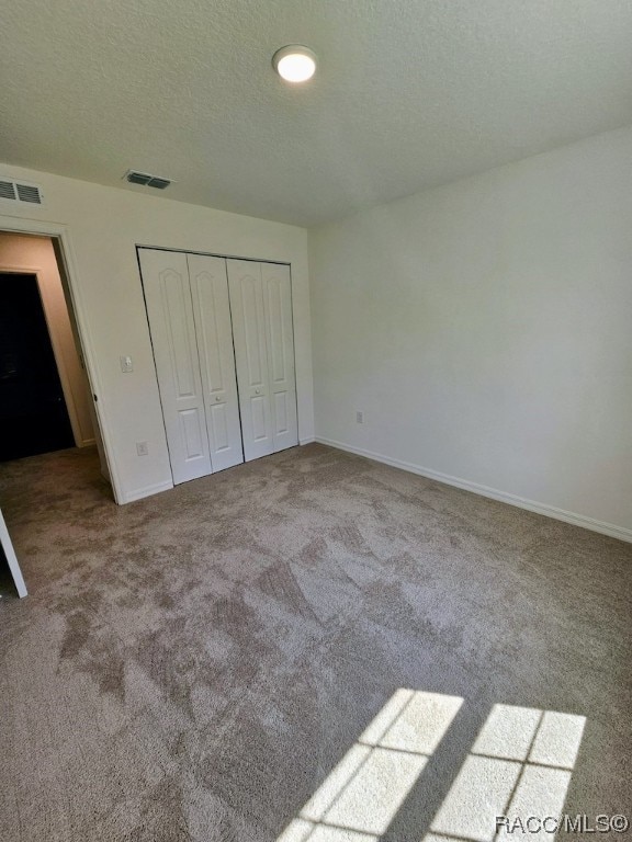 unfurnished bedroom featuring a textured ceiling, light colored carpet, and a closet