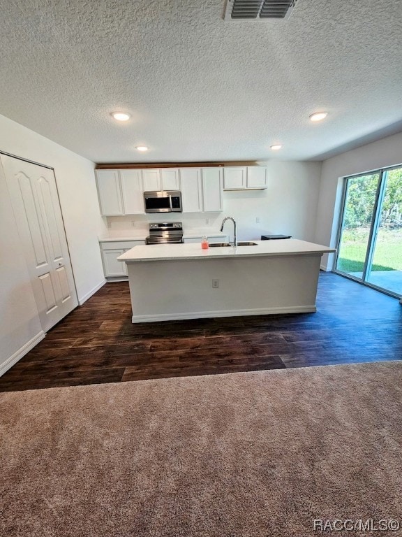 kitchen featuring white cabinets, stainless steel appliances, dark wood-type flooring, and a center island with sink