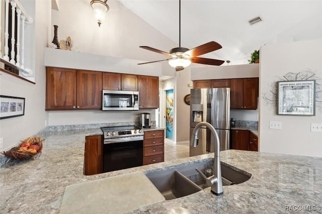 kitchen featuring vaulted ceiling, appliances with stainless steel finishes, light tile patterned floors, light stone counters, and ceiling fan