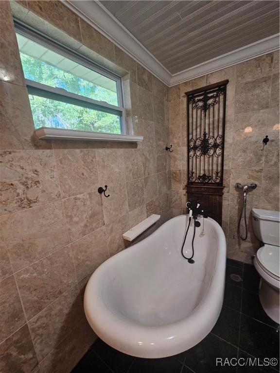 bathroom featuring tile patterned floors, toilet, a bathtub, tile walls, and ornamental molding