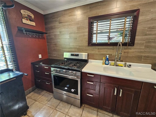 kitchen with ornamental molding, sink, light tile patterned floors, and stainless steel gas range