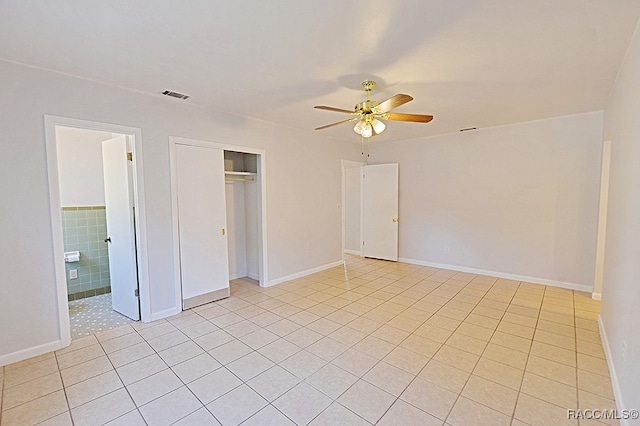 unfurnished bedroom featuring a closet, tile walls, ceiling fan, and light tile patterned flooring