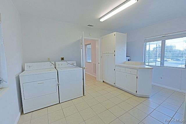 clothes washing area featuring washer and clothes dryer, light tile patterned flooring, and cabinets