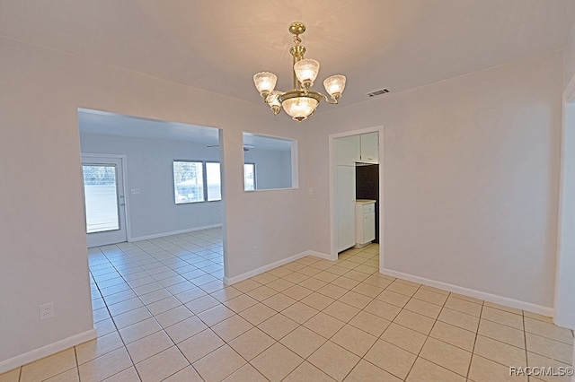 tiled spare room featuring an inviting chandelier