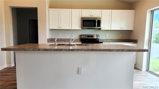 kitchen featuring appliances with stainless steel finishes, a kitchen island with sink, sink, light hardwood / wood-style flooring, and white cabinets