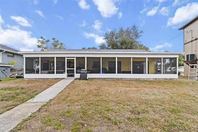 back of house with central AC unit, a sunroom, and a lawn