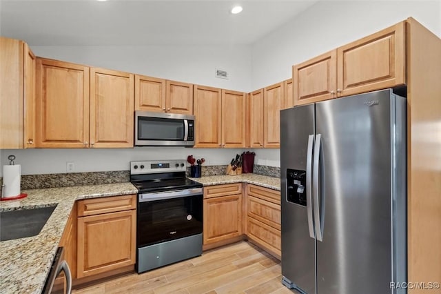 kitchen featuring lofted ceiling, appliances with stainless steel finishes, light stone counters, light brown cabinets, and light wood-type flooring