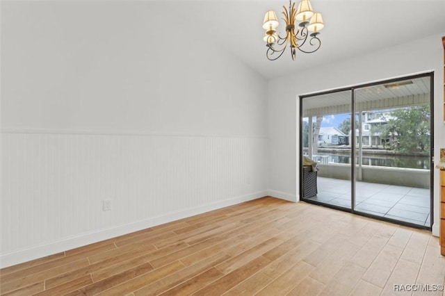 spare room with a water view, vaulted ceiling, light hardwood / wood-style flooring, and a notable chandelier