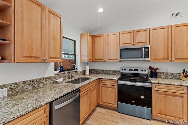 kitchen featuring vaulted ceiling, light stone countertops, appliances with stainless steel finishes, and sink