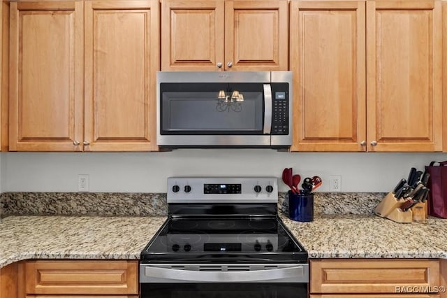 kitchen with stainless steel appliances, light stone countertops, and an inviting chandelier