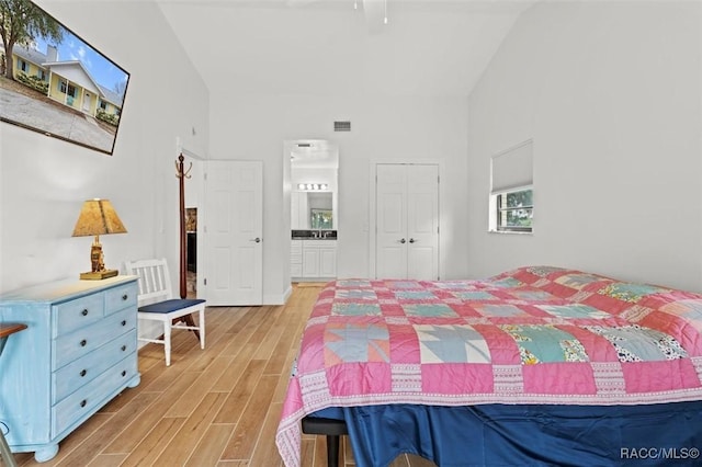 bedroom with high vaulted ceiling, light wood-type flooring, and a closet