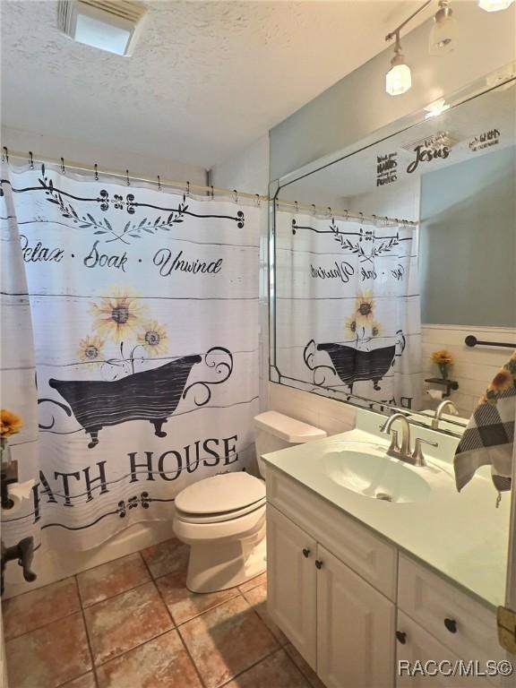 full bathroom featuring vanity, tile patterned floors, toilet, shower / bath combo with shower curtain, and a textured ceiling