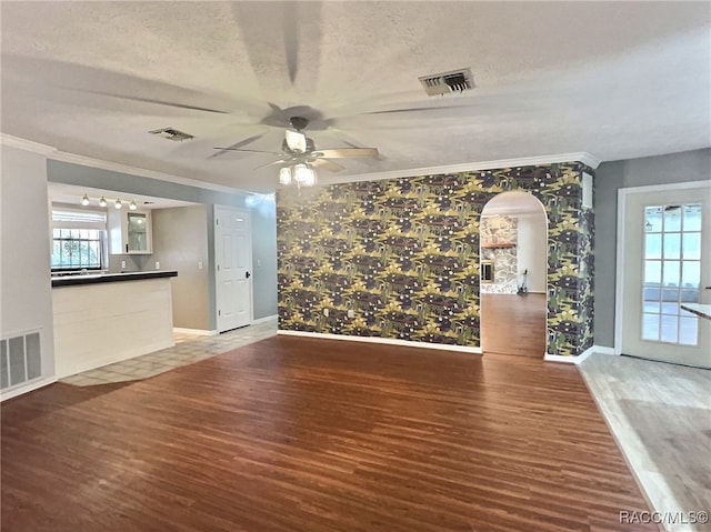 unfurnished living room with ceiling fan, ornamental molding, a textured ceiling, and hardwood / wood-style flooring