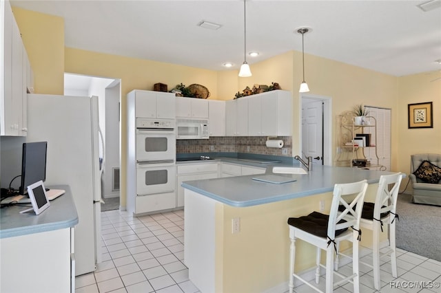 kitchen with a breakfast bar, a sink, white appliances, a peninsula, and light tile patterned floors