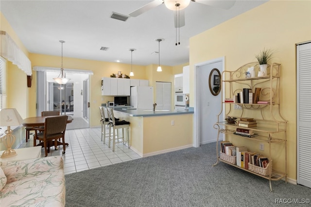 kitchen featuring a breakfast bar, white appliances, a ceiling fan, white cabinetry, and visible vents