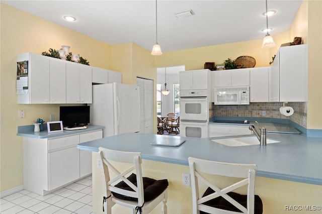 kitchen featuring white appliances, decorative light fixtures, a sink, and a kitchen bar