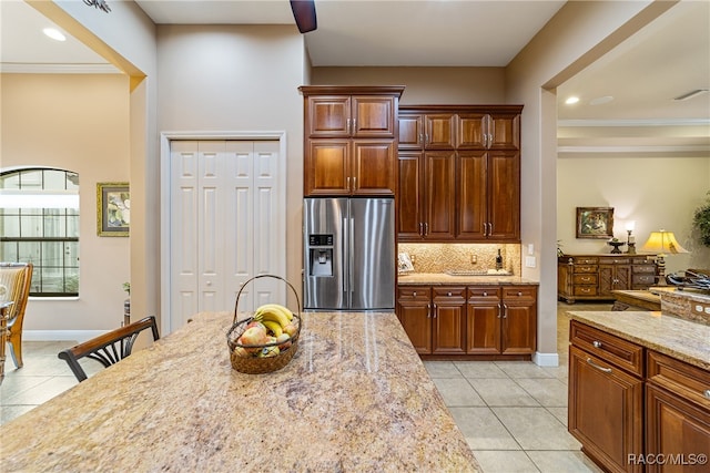 kitchen featuring a kitchen breakfast bar, stainless steel refrigerator with ice dispenser, crown molding, light tile patterned flooring, and light stone counters