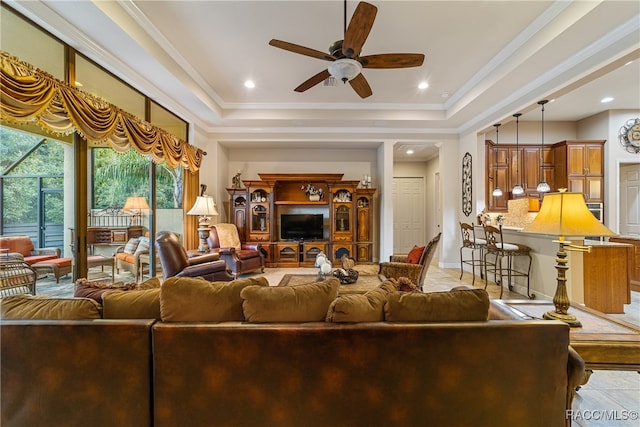 living room with a raised ceiling, ceiling fan, and ornamental molding