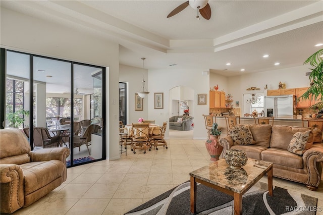 living room with light tile patterned floors, a ceiling fan, recessed lighting, arched walkways, and a raised ceiling